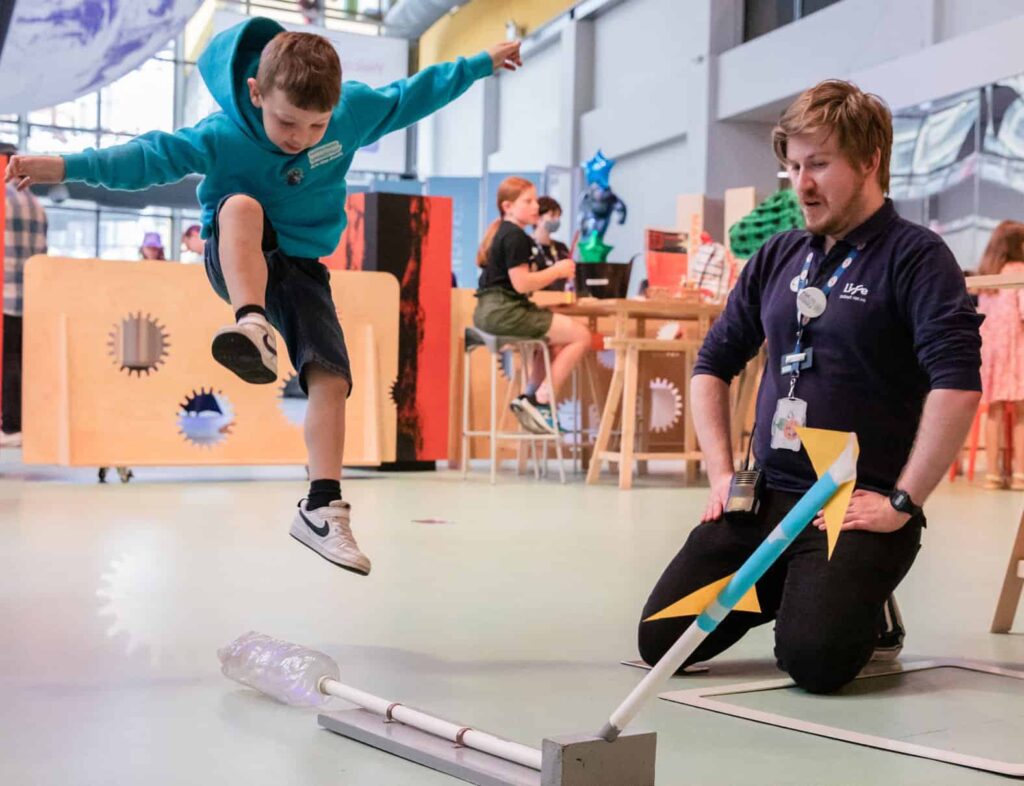 Explainer Assisting Young Visitor With Rocket Launcher In Making Studios.
