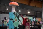 Young teen with grandad looking at large mushroom in Life Science Centre exhibit.