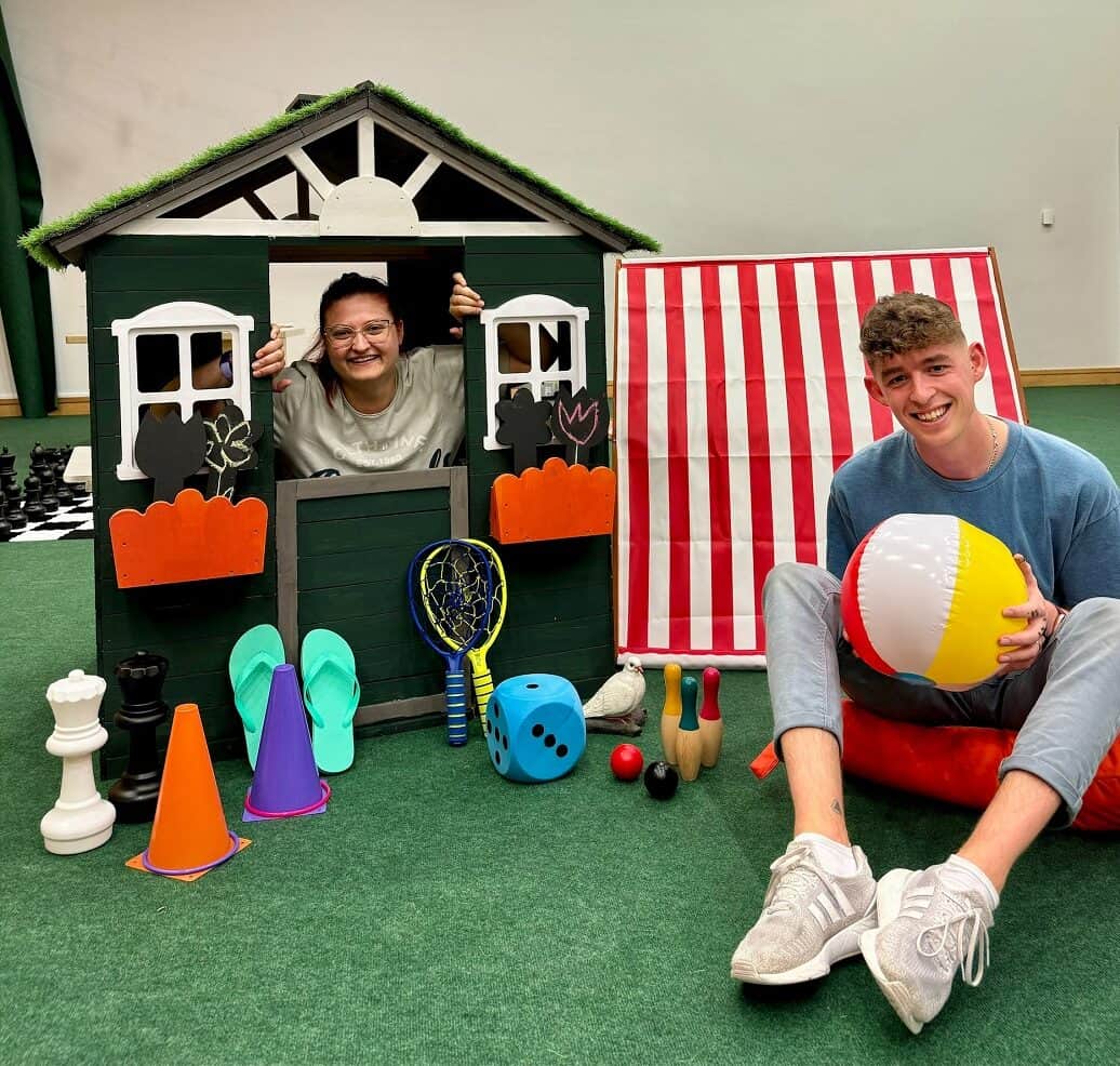 Two team members in wendyhouse with summer activities surrounding them such as beach balls and giant chess pieces.