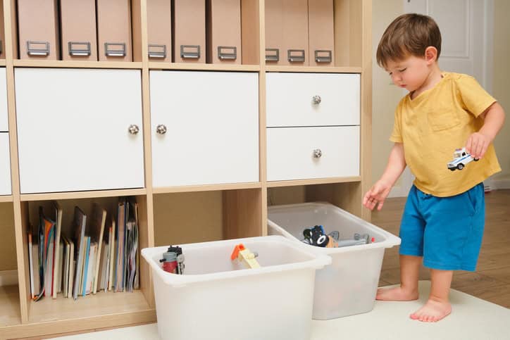 Baby is happily picking up and collecting his toys for cleaning. Kid toddler boy aged two years