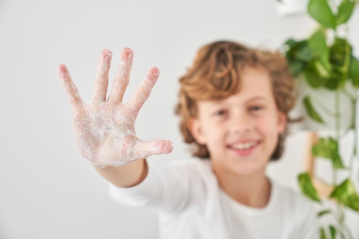 Selective focus of palm of cheerful boy cleaning hands with soap while doing daily hygiene routine in morning