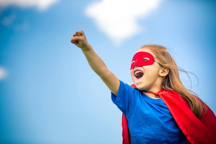 Funny little girl playing power super hero over blue sky background. Superhero concept.