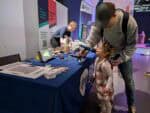 Little girl talking in mic with assistance of dad wearing a cap in science centre.