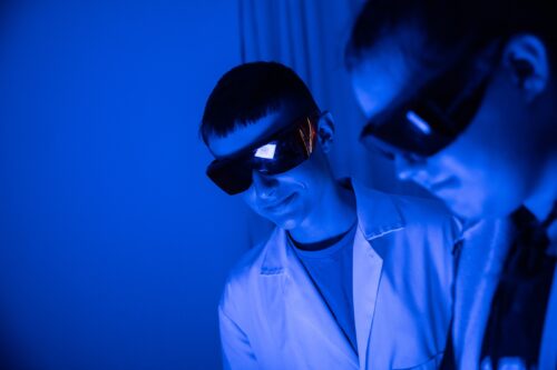 Teenagers in science workshop wearing lab coats and safety goggles.