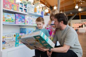 Two children in Life Science Centre's gift shop looking at boxed actvity for sale with father.