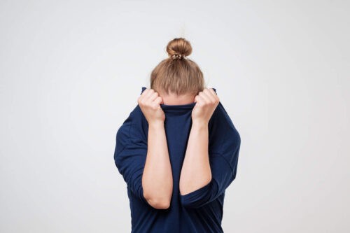 European Woman Hiding Face Under The Clothes. She Is Oulling Sweater On Her Head.