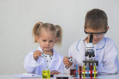 Cute Children In Lab Coats Playing With Microscope And Test Tubes.