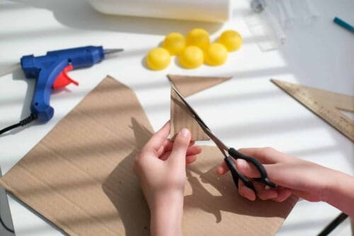 A young child's hands using scissors to cut cardboard to make a boat.