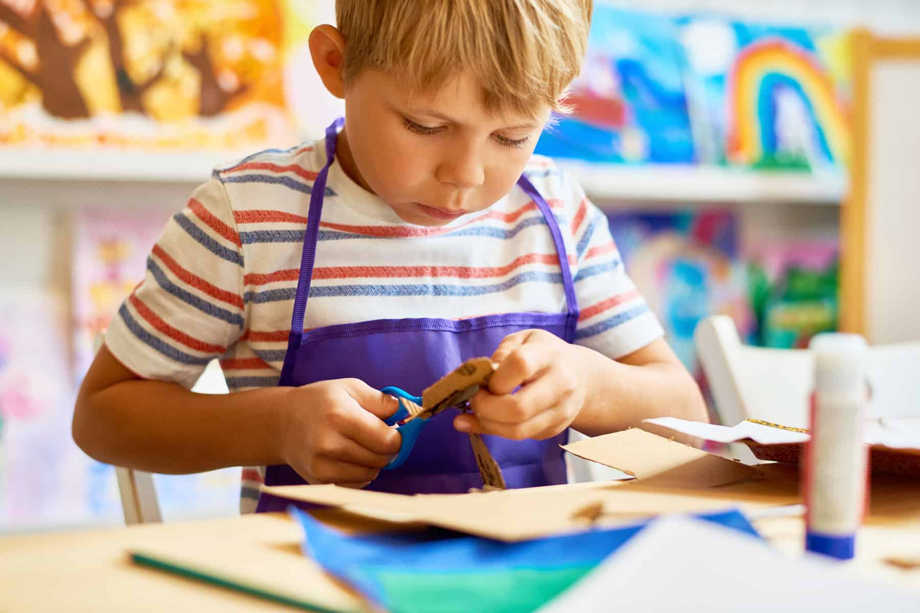 A young child cutting cardboard to make a boat.