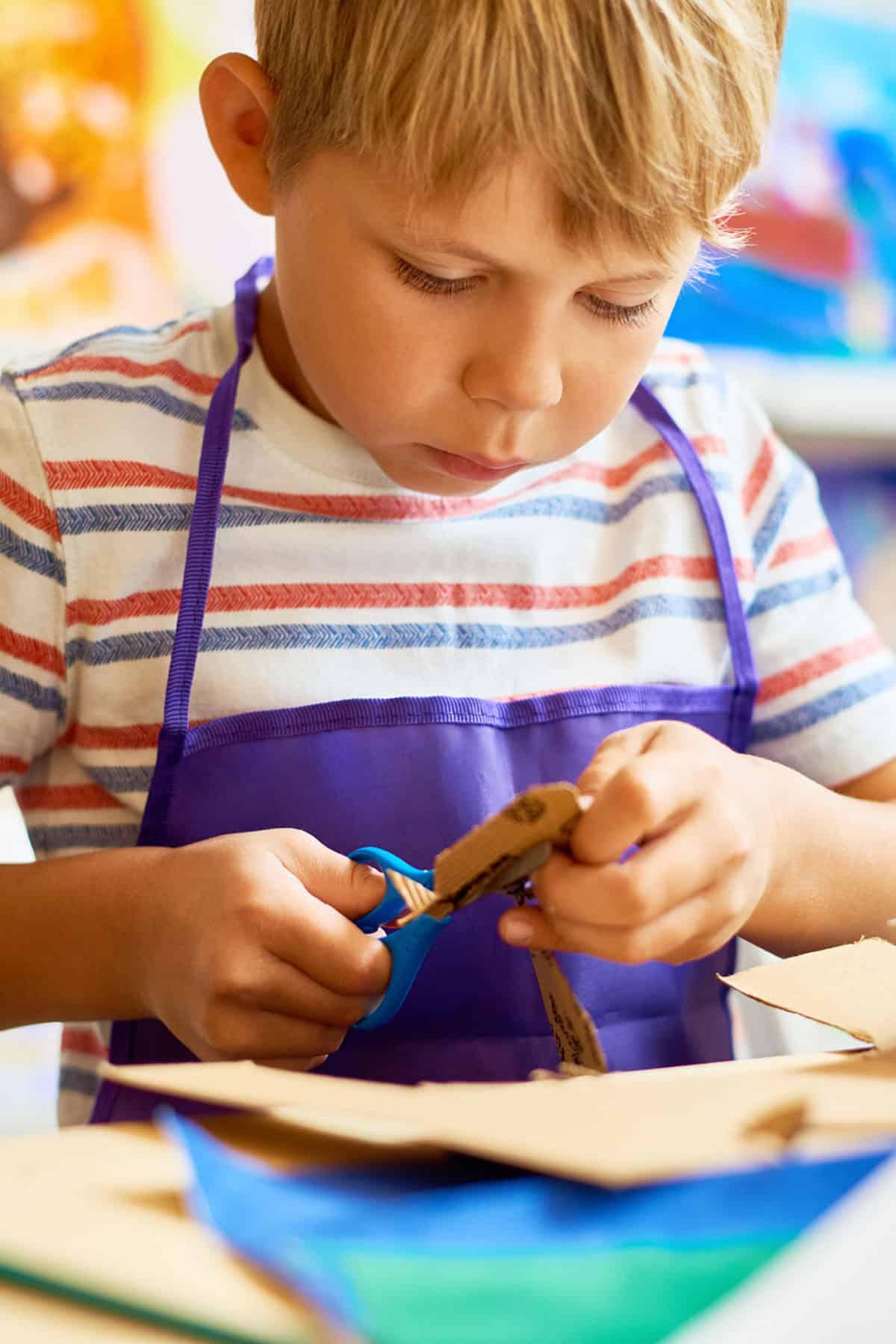 A young child cutting cardboard to make a boat.
