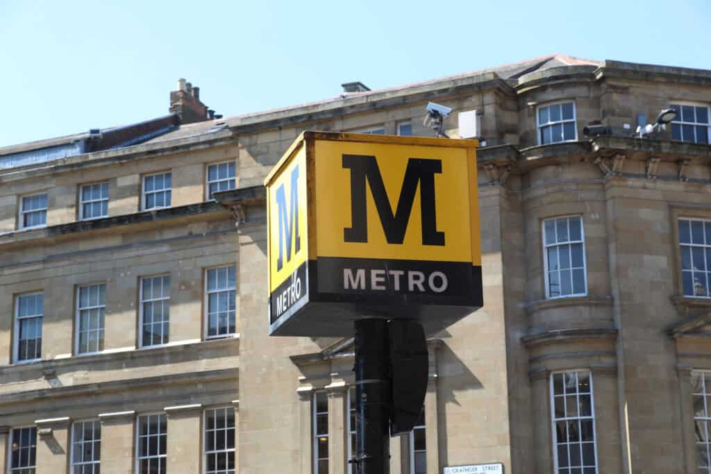 Large yellow Metro station totem pole on grey street.