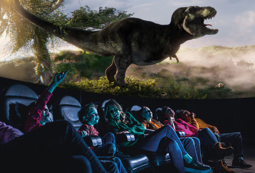 Family looking up in Life Science Centre's planetarium at large T. Rex dinosaur.