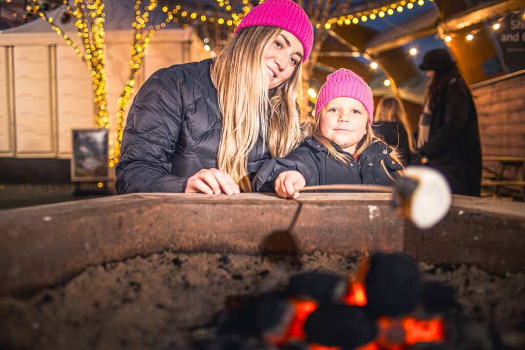 Mother and daughter toasting marshmallows on ourdoor firepit at Life Science Centre ice rink.