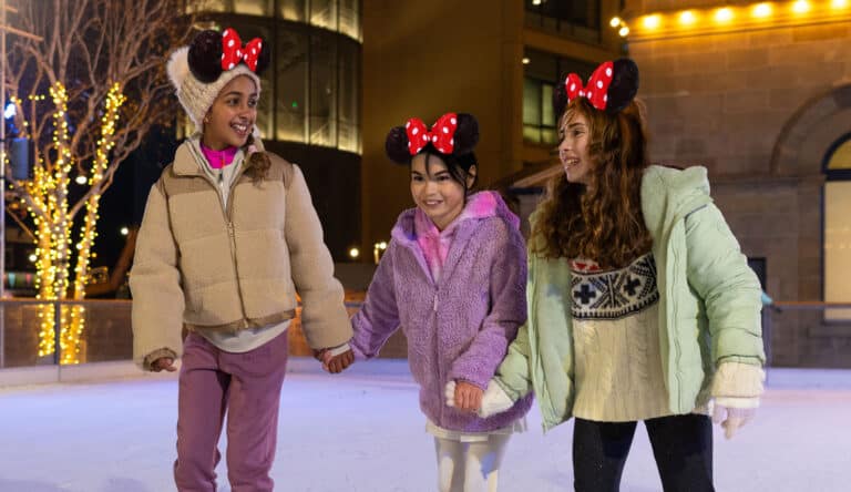 Three girls on Life Science Centre's outdoor ice rink skating whilst wearing Disney mouse ears.