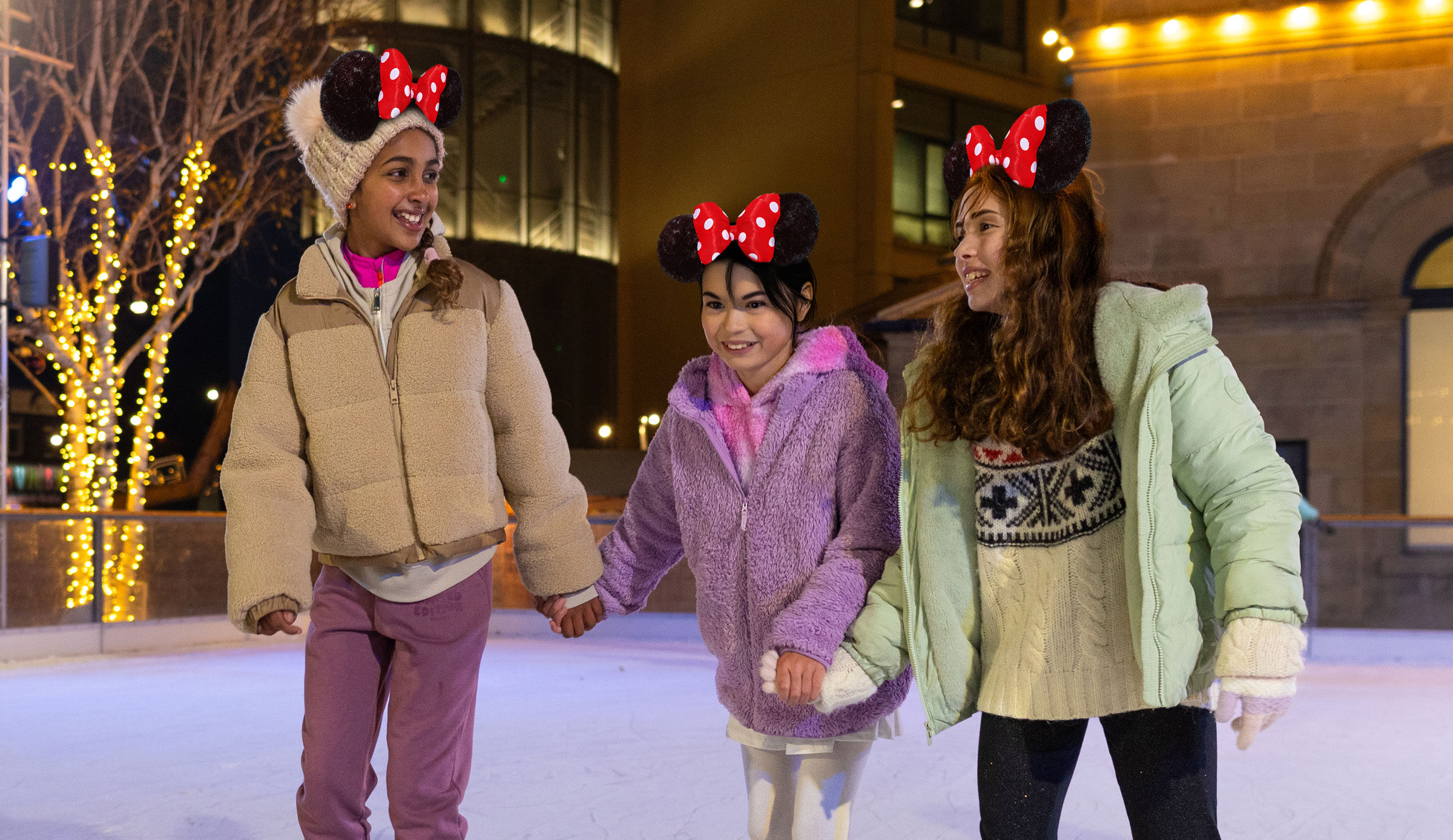 Three girls on Life Science Centre's outdoor ice rink skating whilst wearing Disney mouse ears.