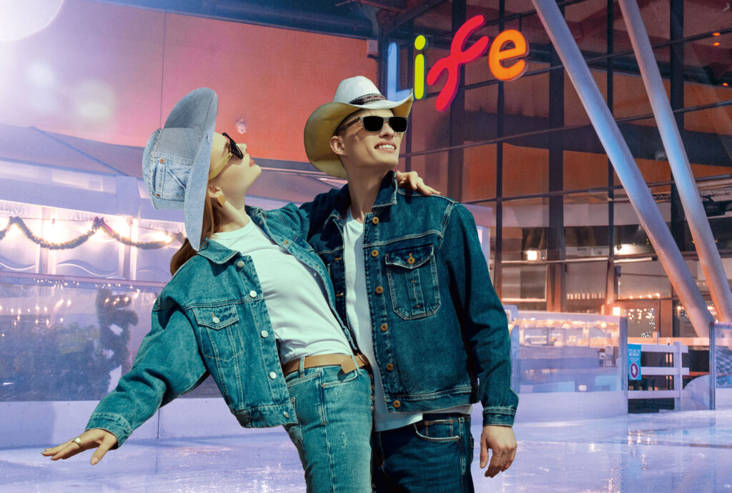 Two adults wearing noughties inspired double denim, cowboy hats and sunglasses on Newcastle's outdoor ice rink in front of Life Science Centre.