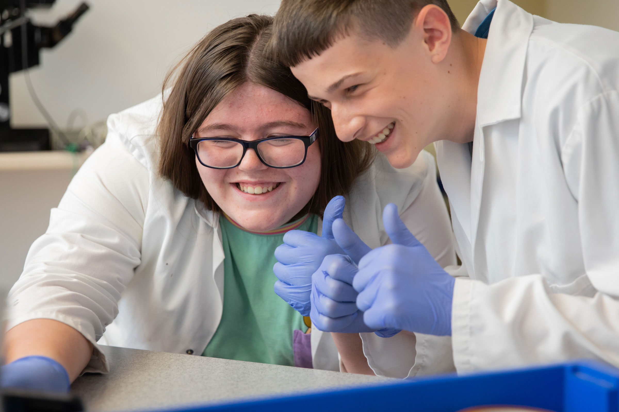 Two students in forensic DNA workshop completing experiment in white lab coat and blue gloves at Life Science Centre.