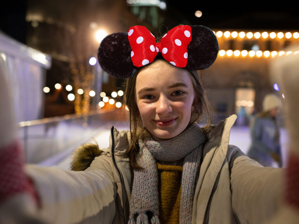 Young girl wearing disney mouse ears holding a camera and smiling whilst on Life Science Centre ice rink.