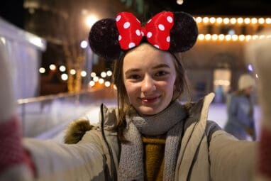 Young girl wearing disney mouse ears holding a camera and smiling whilst on Life Science Centre ice rink.