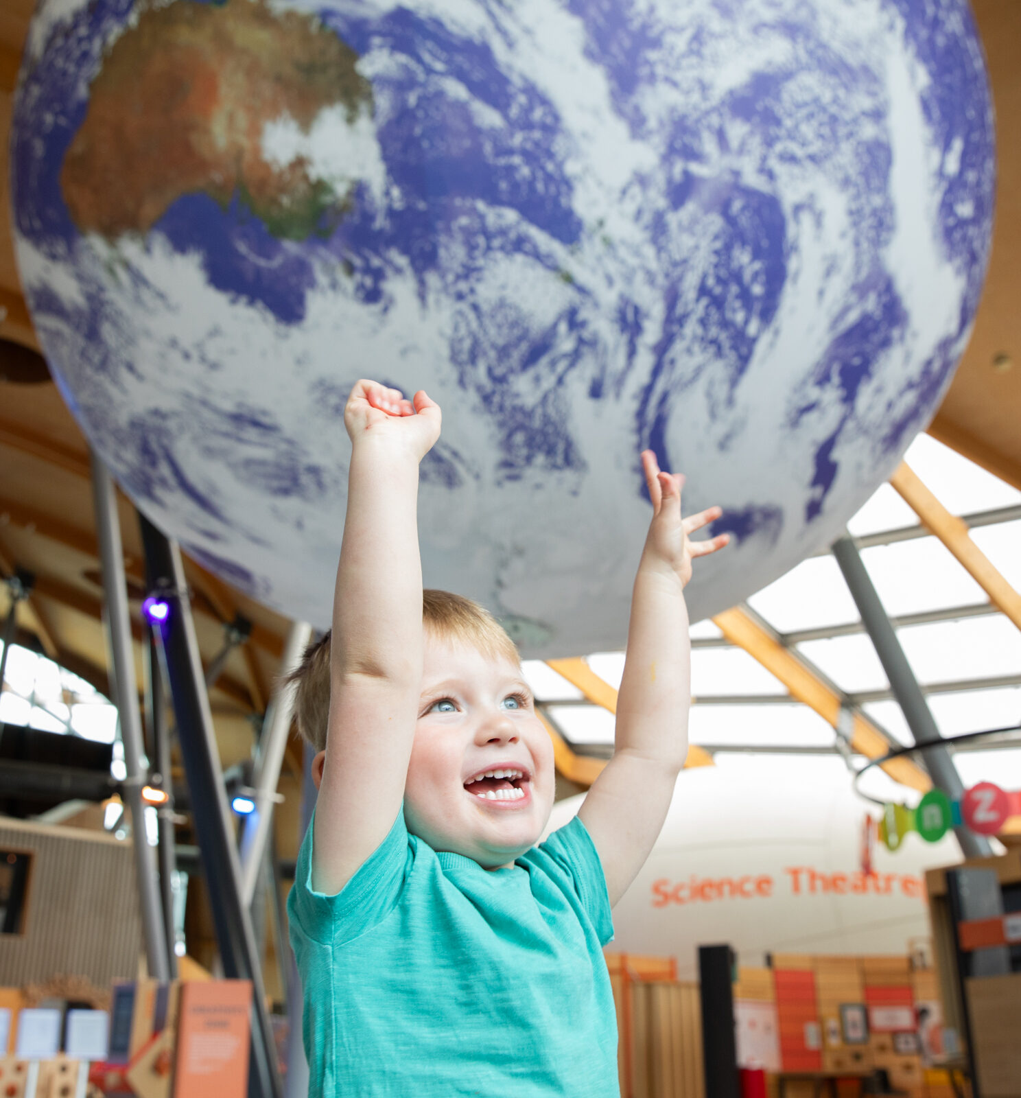 Young toddler with arms outstretched and smiling in front of Gaia, Life Science Centre's replica of Planet Earth.