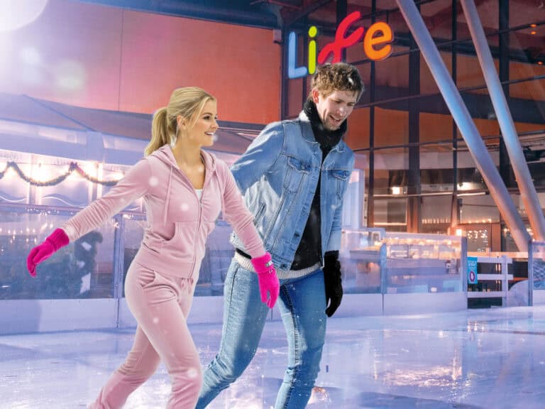 Couple dressed in noughties inspired clothing on Life Science Centre ice rink in Newcastle. The woman is wearing a pink tracksuit whilst the man is in double denim.