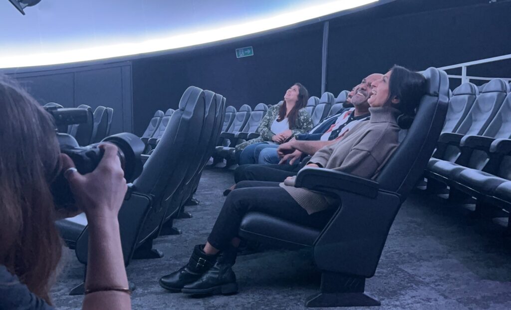 Photographer in Life Science Centre's Planetarium taking a photo of a family sat down and looking up at domed screen.