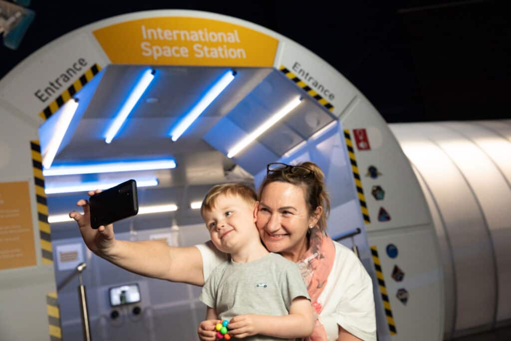 Grandma And Child In Life Science Centre's Space Zone Taking A Selfie In Front Of The Model International Space Station