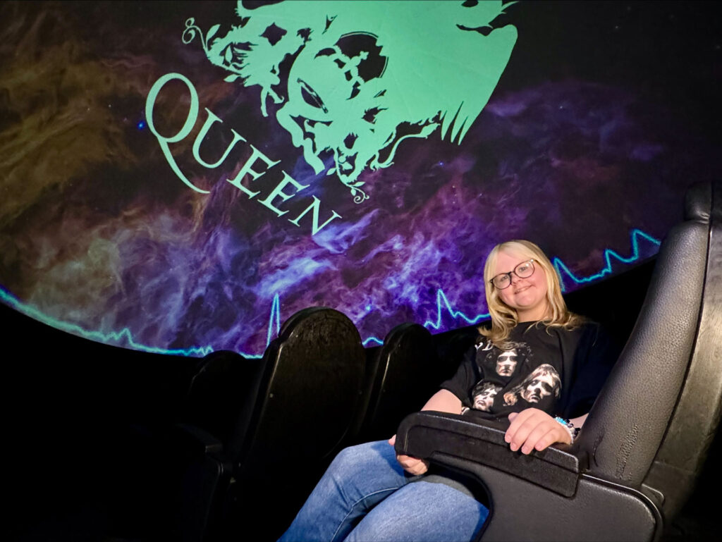 Young girl sat in Life's Planetarium, watching Queen Heaven planetarium show, wearing a Queen T-shirt