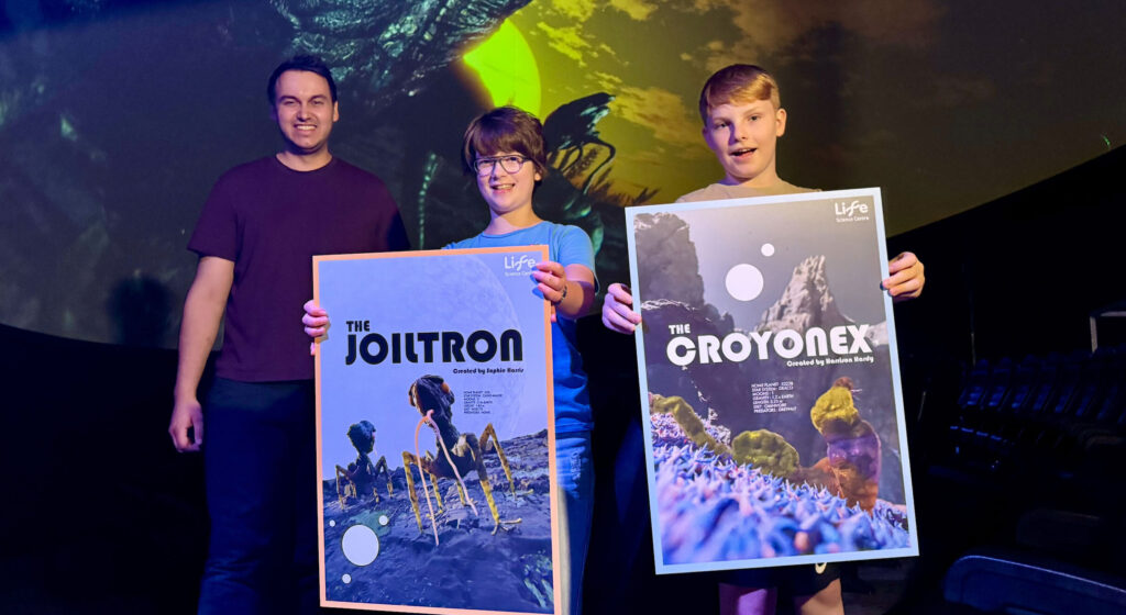 Sophie Harris and Harrison Hardy holding posters of their aliens in Life Science Centre's Planetarium.