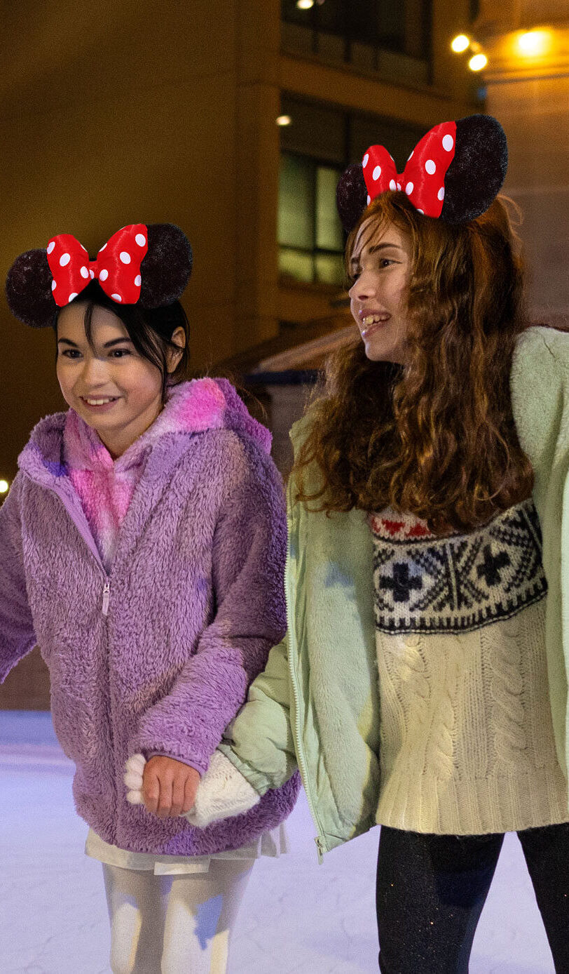 Three girls on Life Science Centre's outdoor ice rink skating whilst wearing Disney mouse ears.