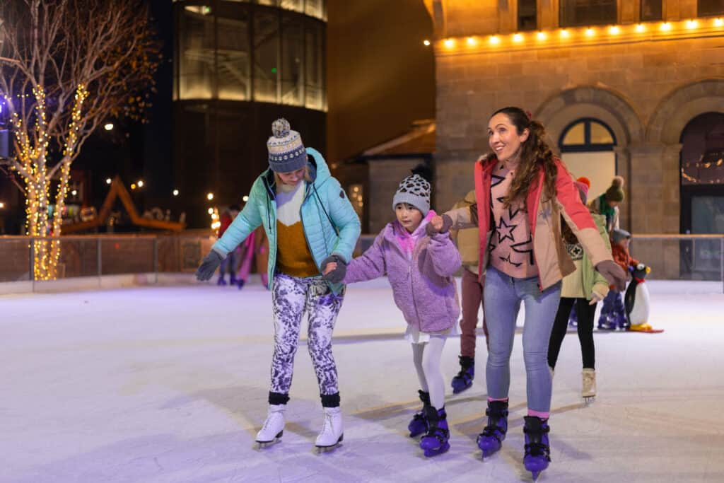 Two adults and child holding hands whilst skating on Newcastle's outdoor ice rink