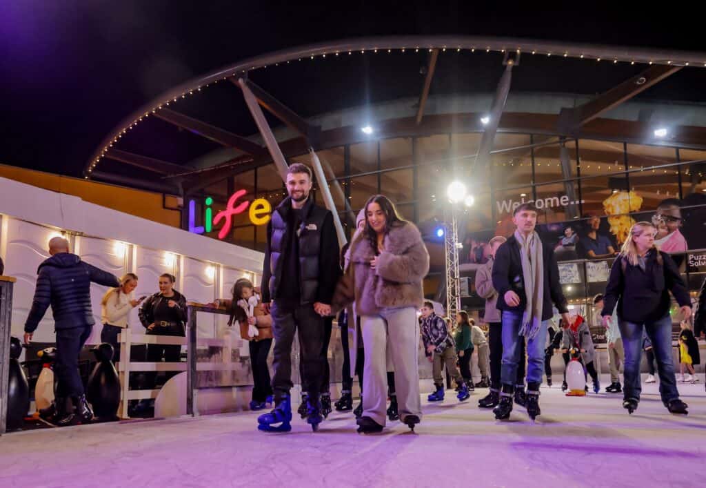 Couple holding hands whilst skating at outdoor rink.