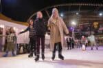 Mum and daughter holding hands whilst skating at outdoor ice rink.