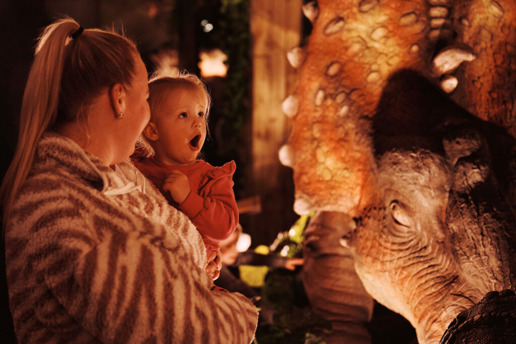 Little Girl Being Held By Mum Looking Amazed At A Stegasaurus.