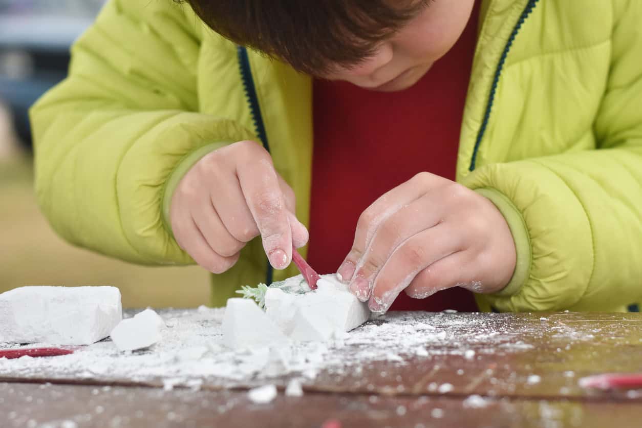 Boy plays as a palaeontologist, digging out a toy dinosaur from a clay block