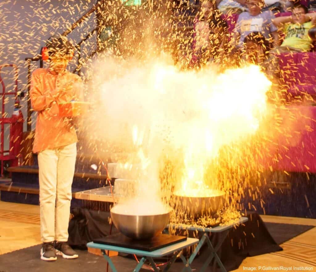 Young child wearing ear defenders looking shocked in front of an explosion at Newcastle's Life Science Centre. 