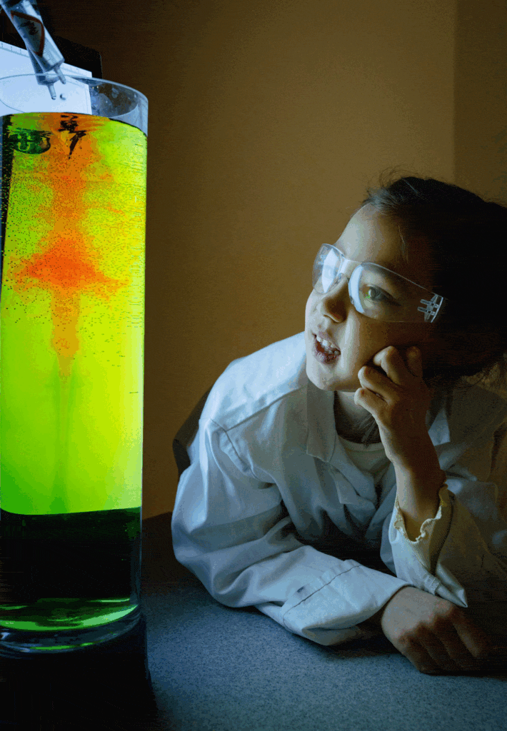 Little girl looking in lab coat looking at swirling brightly coloured liquid during Life Science Centre practical schools workshop.