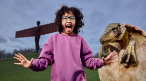 Little girl screaming next to dinosaur in egg in front of Gateshead's The Angel of the North