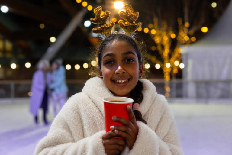 Little girl wearing a dressing gown and holding a hot chocolate on Newcastle's outdoor ice rink.
