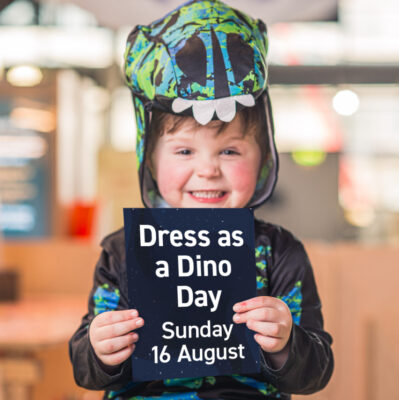 Little boy in dinosaur costume holding a sign.