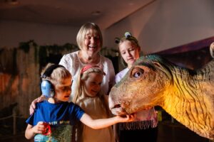 Gradmother with three grandchildren smiling at baby stegasaurus at Newcastle's Life Science Centre.