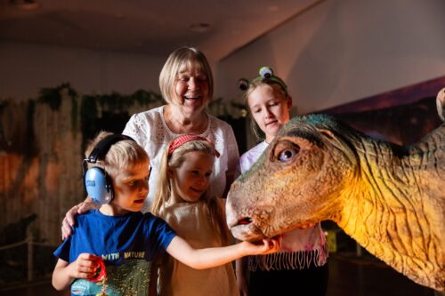 Gradmother with three grandchildren smiling at baby stegasaurus at Newcastle's Life Science Centre.