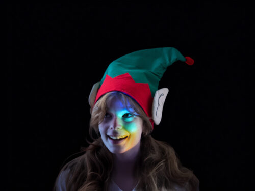 A Christmas elf staring up in wonder as lots of different colours land on her face
