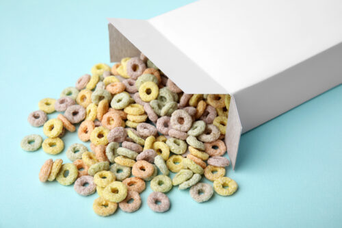 Paper box with tasty cereal rings on light blue background, closeup