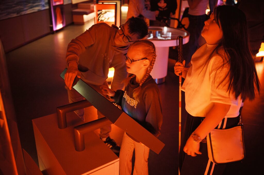 Family enjoying hands-on activity in Life Science Centre's Lightbox. One visitor is using a walking cane.