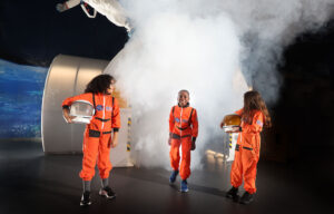 School aged students in Life Science Centre's Space Zone wearing bright orange space suits and holding helmets.